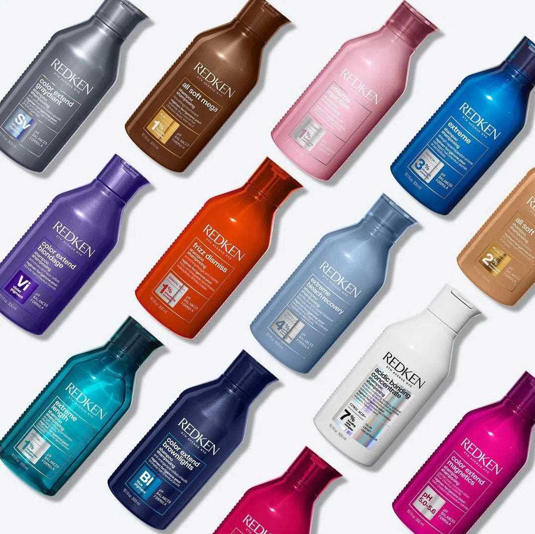 Redken shampoo and conditioner bottles in assorted colors arranged diagonally on a light background.